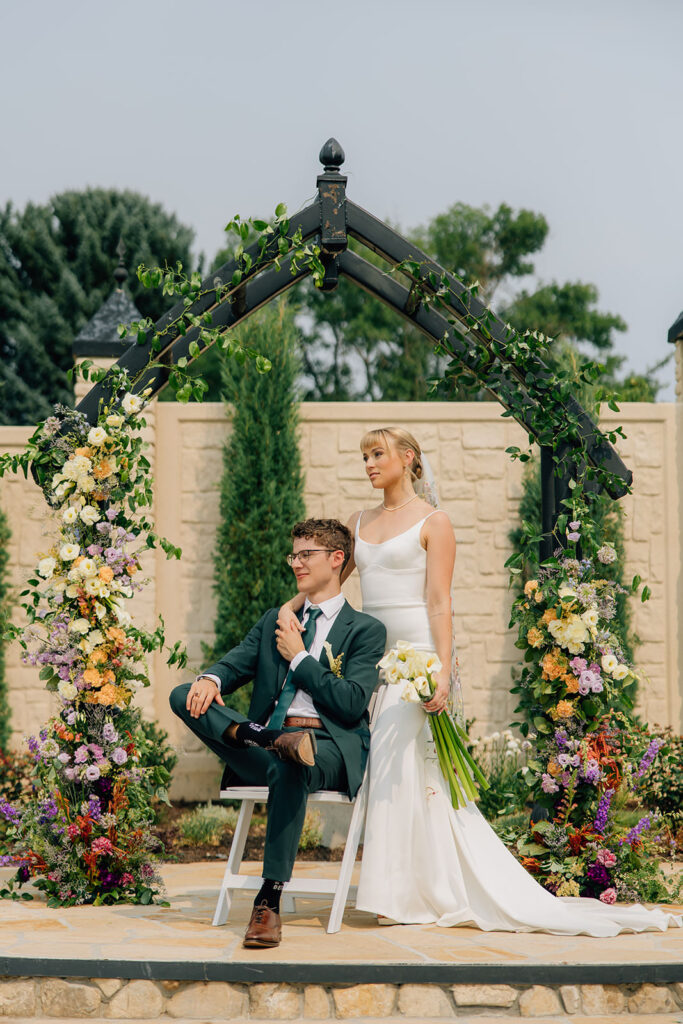 groom sitting in a chair and bride standing next to him.