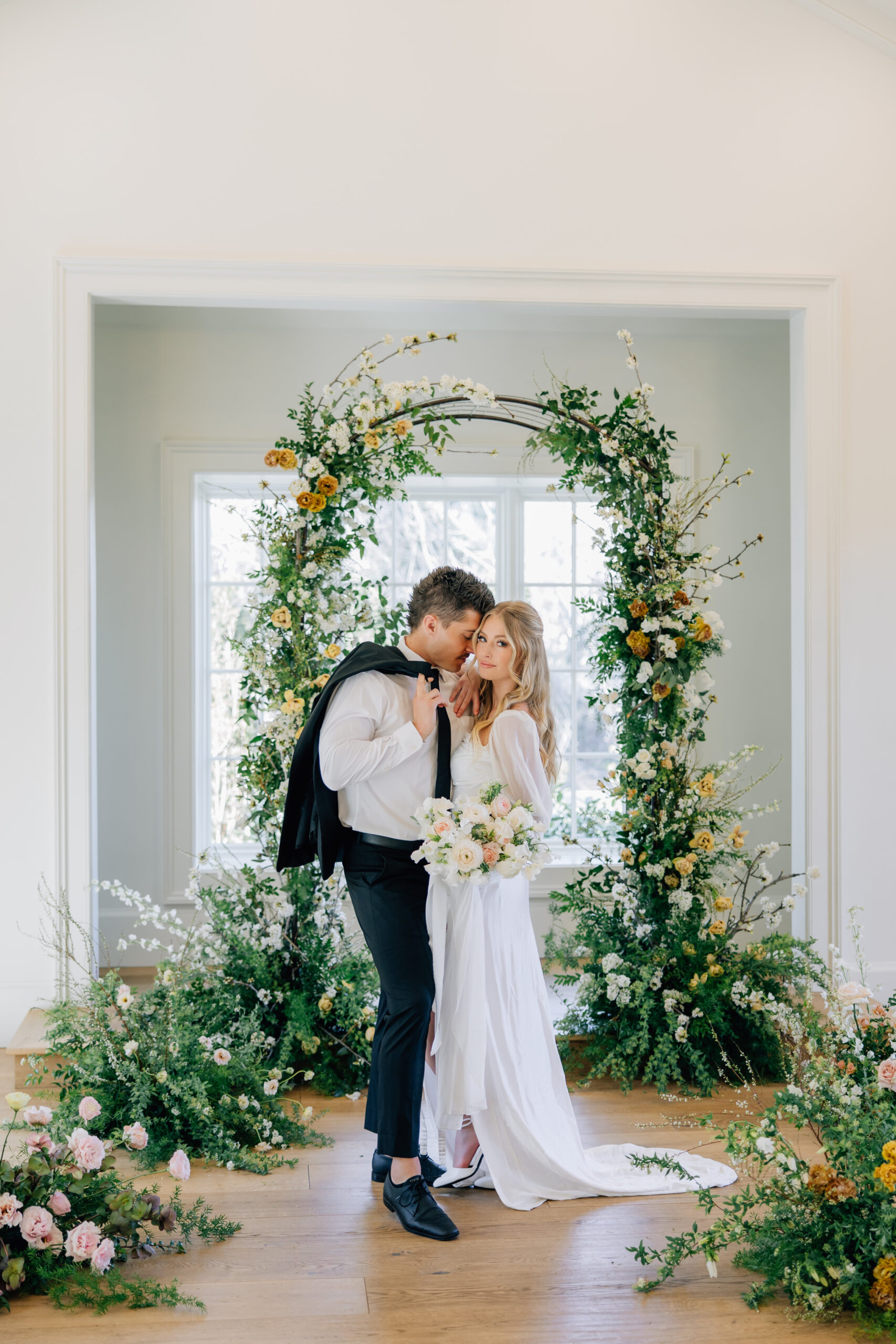 bride and groom in front of floral arch